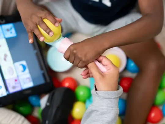 A child playing during an ABA therapy session while a registered behavior technician uses a tablet to track progress.