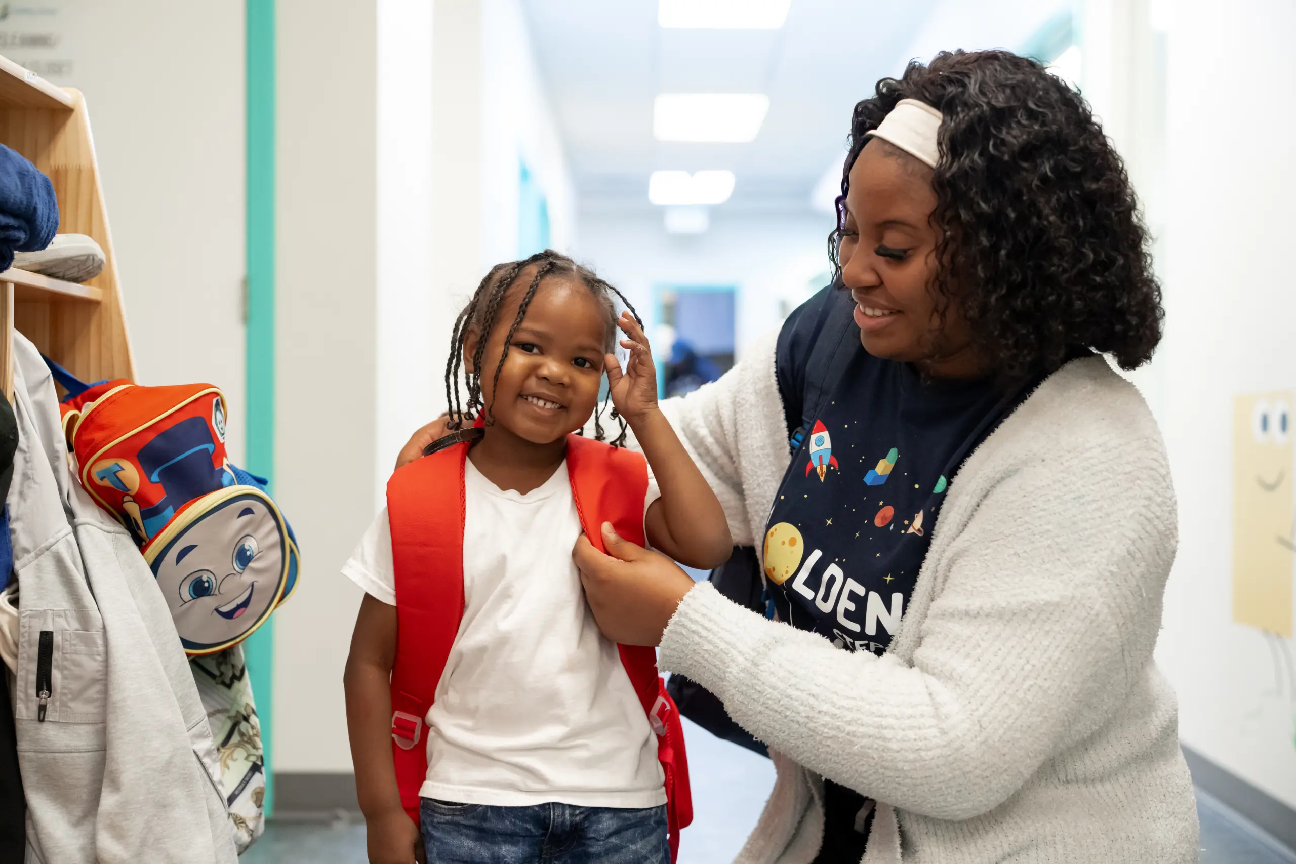 Smiling child receiving help from an RBT while putting on a backpack